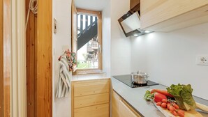 A kitchen with wooden cabinets, a window, a pot on the stove, and fresh vegetables on the counter. - Appartamento Vecchio Gad (Oulx)