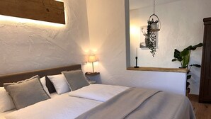A neatly made bed with a headboard, a bedside lamp, and a wall-mounted mirror with a hanging plant. - Apartment Liesl 75sqm for max. 5 persons (Schechen)