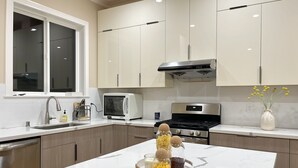 A modern kitchen with white cabinets, a stainless steel stove, and a marble countertop.
