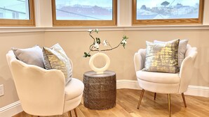A room with two white armchairs, a round wooden side table, and a wall-mounted orchid plant.
