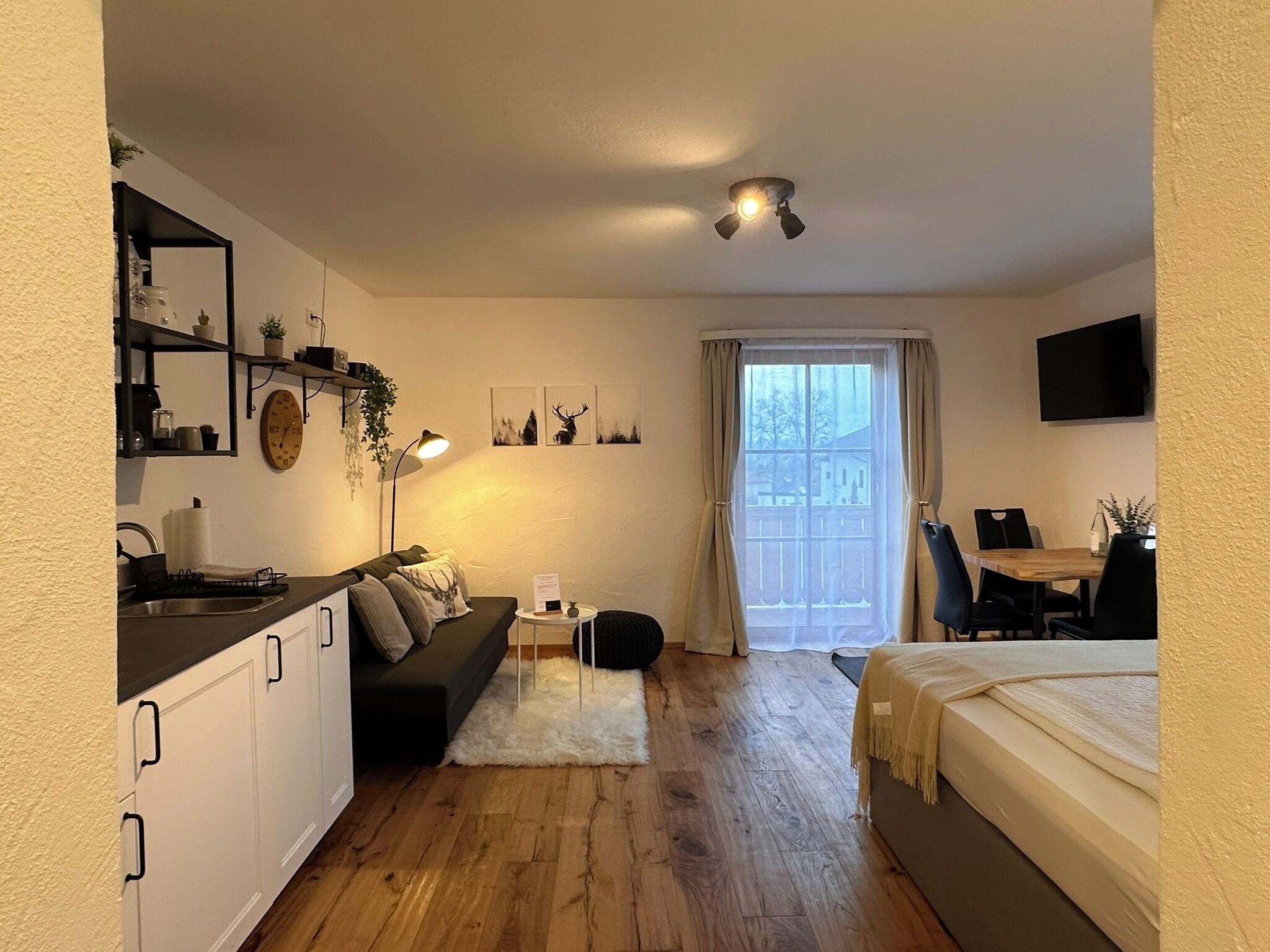 Ein kompakter Wohnbereich mit Küchenzeile, einer Couch, einem Esstisch und einem Bett.