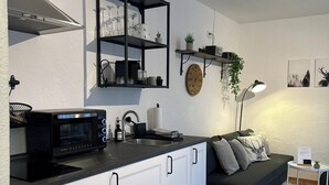 A modern kitchen with white cabinets, a black countertop, and a built-in microwave. There is a black shelf above the counter holding various items. - Apartment Rosa 35sqm with balcony (Schechen)