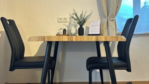 A room with a wooden table, two black chairs, a potted plant, and a flat-screen TV mounted on the wall. - Apartment Rosa 35sqm with balcony (Schechen)