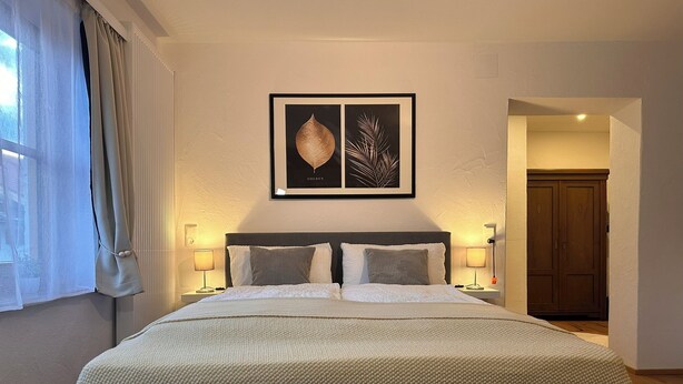 A neatly made bed with a textured blanket, two bedside lamps, and a framed artwork above the bed. - Apartment Rosa 35sqm with balcony (Schechen)