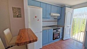 A compact kitchen with blue cabinets, a white refrigerator, a built-in oven, and a small dining table. - El Alfar - Denia, Costa Blanca (Denia)