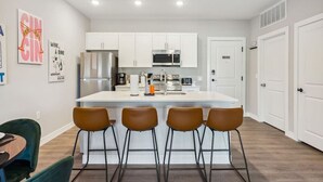 Una cucina moderna con mobili bianchi, un frigorifero in acciaio inossidabile, un forno a microonde e un'isola centrale con sgabelli da bar.