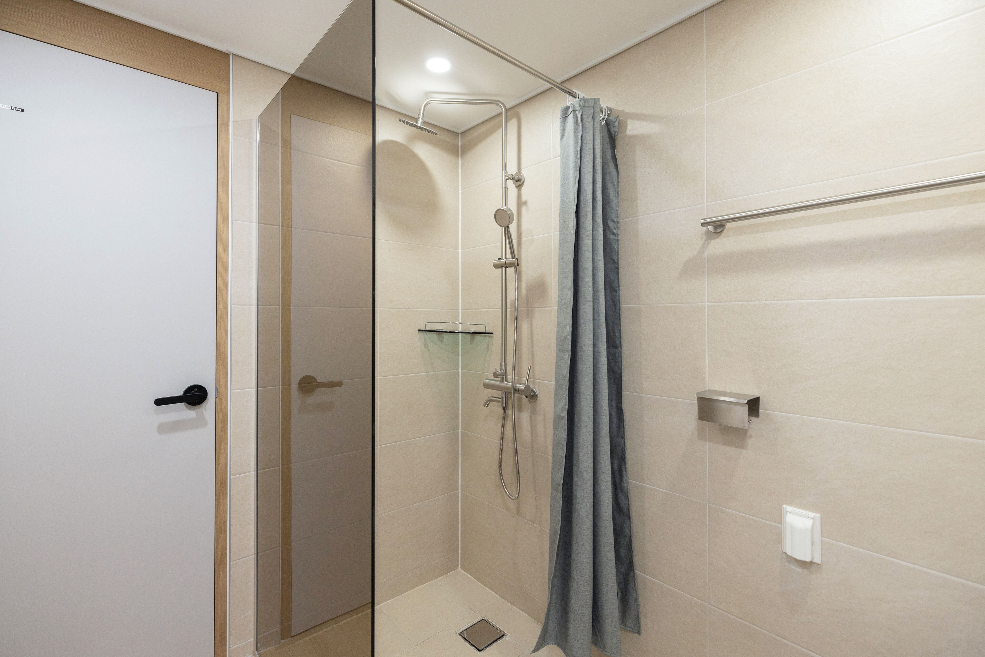 A modern shower area with a glass door, a showerhead, a towel rack, and a glass shelf.