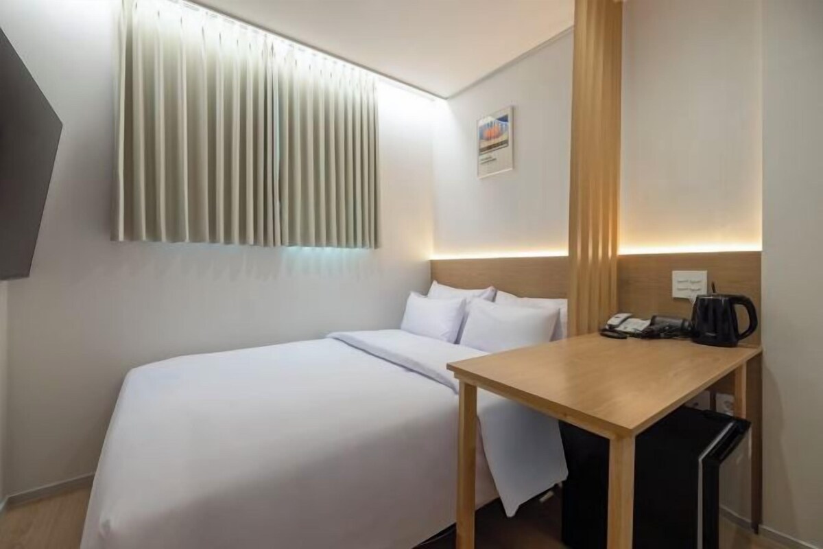 Habitación de hotel con cama, una mesa de madera, cafetera y ventana con persianas.