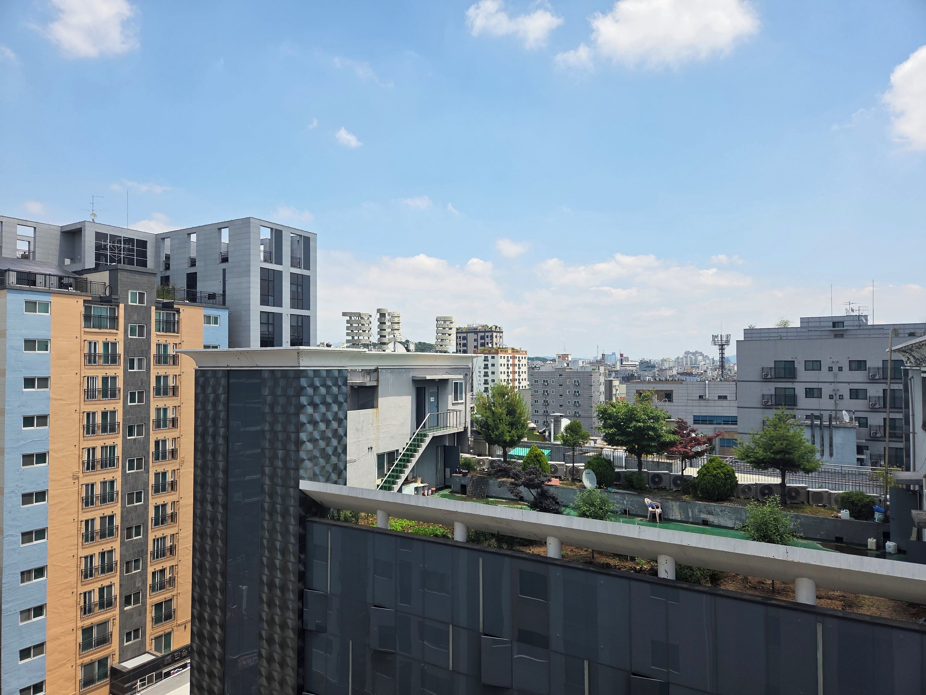 A modern urban landscape with high-rise buildings, a rooftop garden, and a staircase leading to an upper level.
