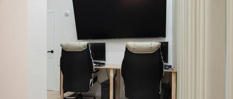 Un espace de bureau moderne, doté de deux chaises de bureau noires, d’un grand téléviseur à écran plat fixé au mur et d’un bureau en bois.
