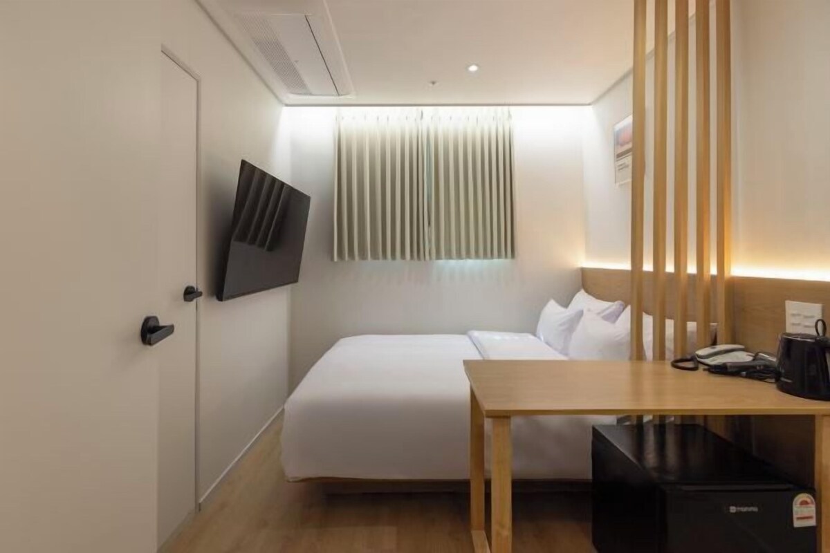 Ein Hotelzimmer mit Bett, Schreibtisch, Fernseher und einem Fenster mit Jalousien.
