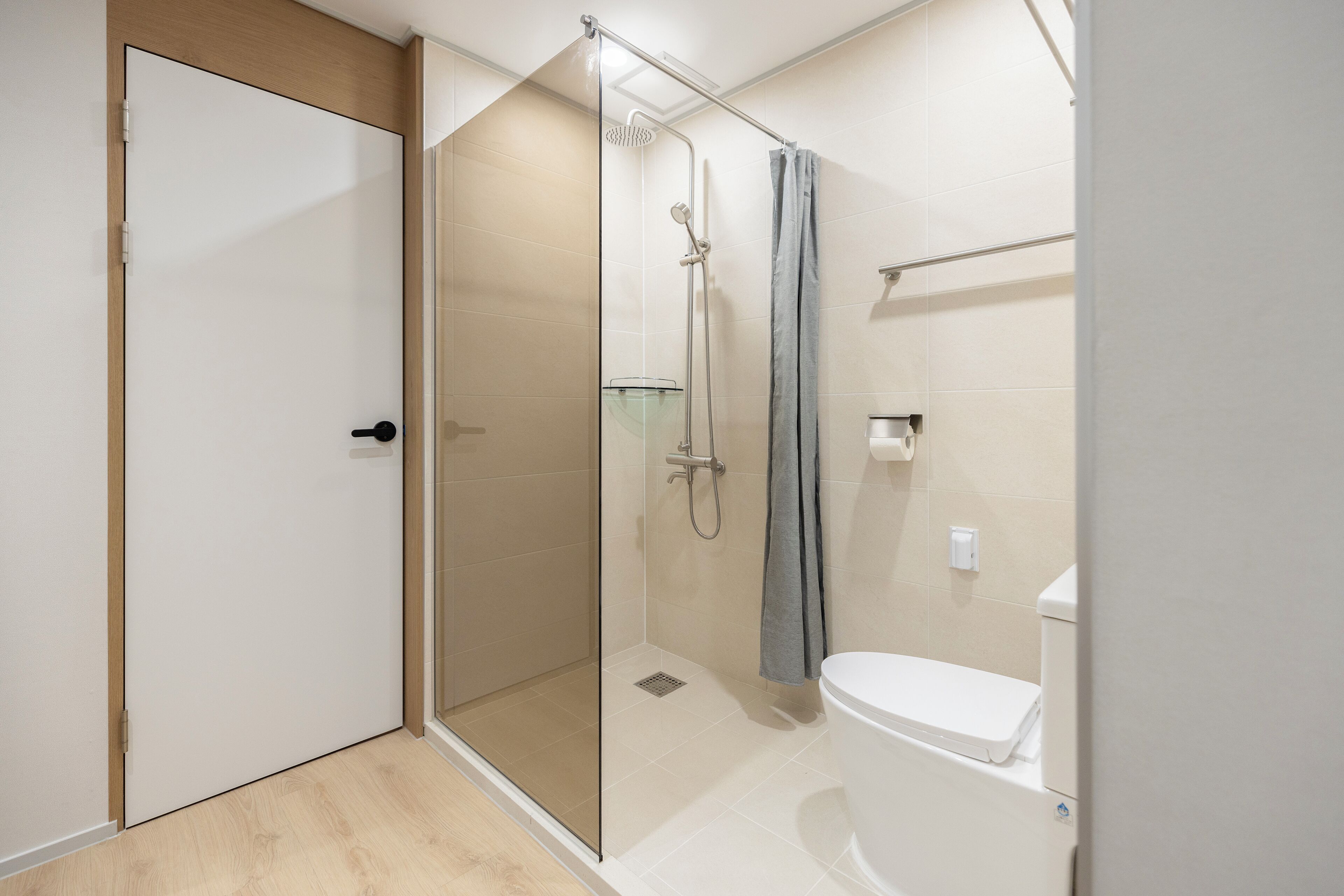 A modern bathroom with a glass-enclosed shower, a toilet, and a wooden door.