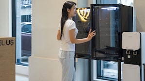 Una persona interactuando con un refrigerador negro en un interior moderno con ventanales grandes.