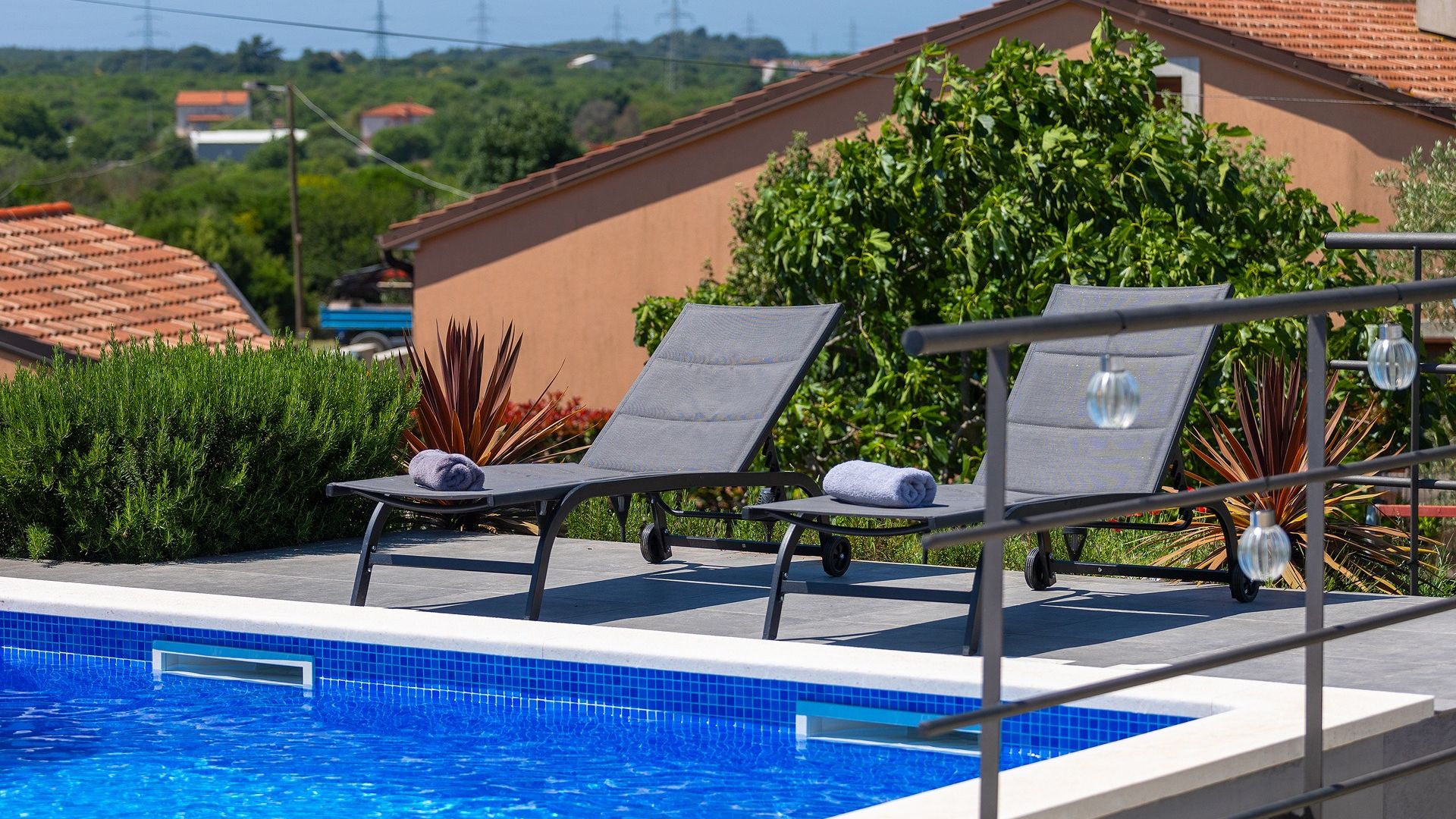 Un espace aménagé au bord de la piscine, avec deux chaises longues, une piscine carrelée et une végétation luxuriante tout autour.