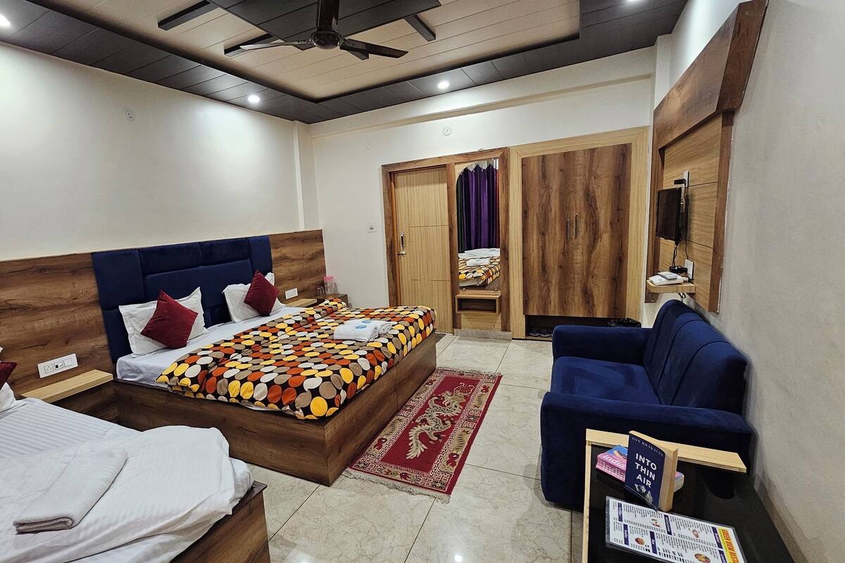 A hotel room with two beds, a sofa, a wardrobe, and a ceiling fan.