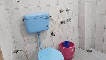 Casa de banho com sanita azul, balde rosa e chuveiro.