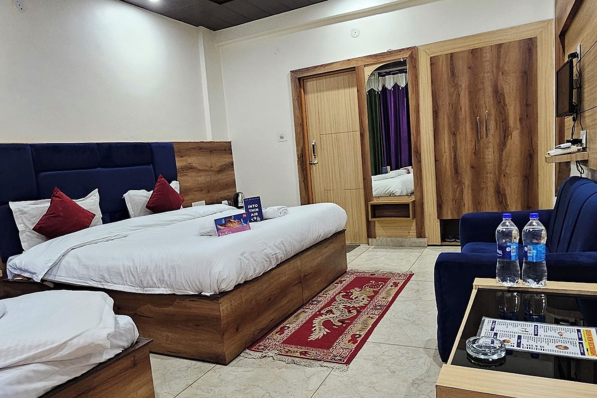 A hotel room with two wooden beds, a red patterned rug, a wooden coffee table, and a blue sofa.