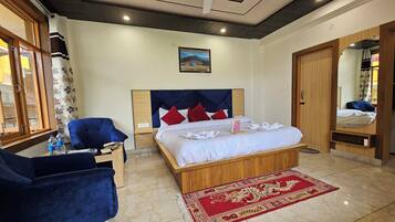 A hotel room with a bed, a blue armchair, a wooden nightstand, a red and beige patterned rug, and a large mirror.