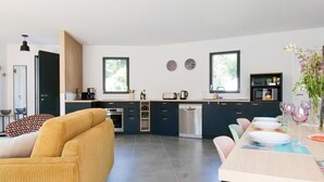 Une cuisine moderne avec des meubles de couleur sombre, un plan de travail en bois et un coin repas avec une table dressée pour quatre personnes.