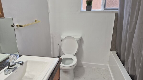 Un baño con inodoro blanco, lavamanos y ventana sobre el inodoro.
