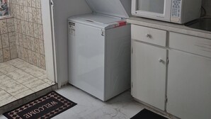 Eine kompakte Küche mit weißen Schränken, einer Mikrowelle, einem Kühlschrank und einer Waschmaschine.