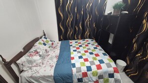 Ein Bett mit einem blumigen und karierten Überwurf, einem Holz-Kopfbrett und einem schwarzen Vorhang mit goldenen Wellenmustern.