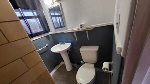 Ein Badezimmer mit weißem Waschbecken, Toilette und einem kleinen Fenster mit Vorhängen.