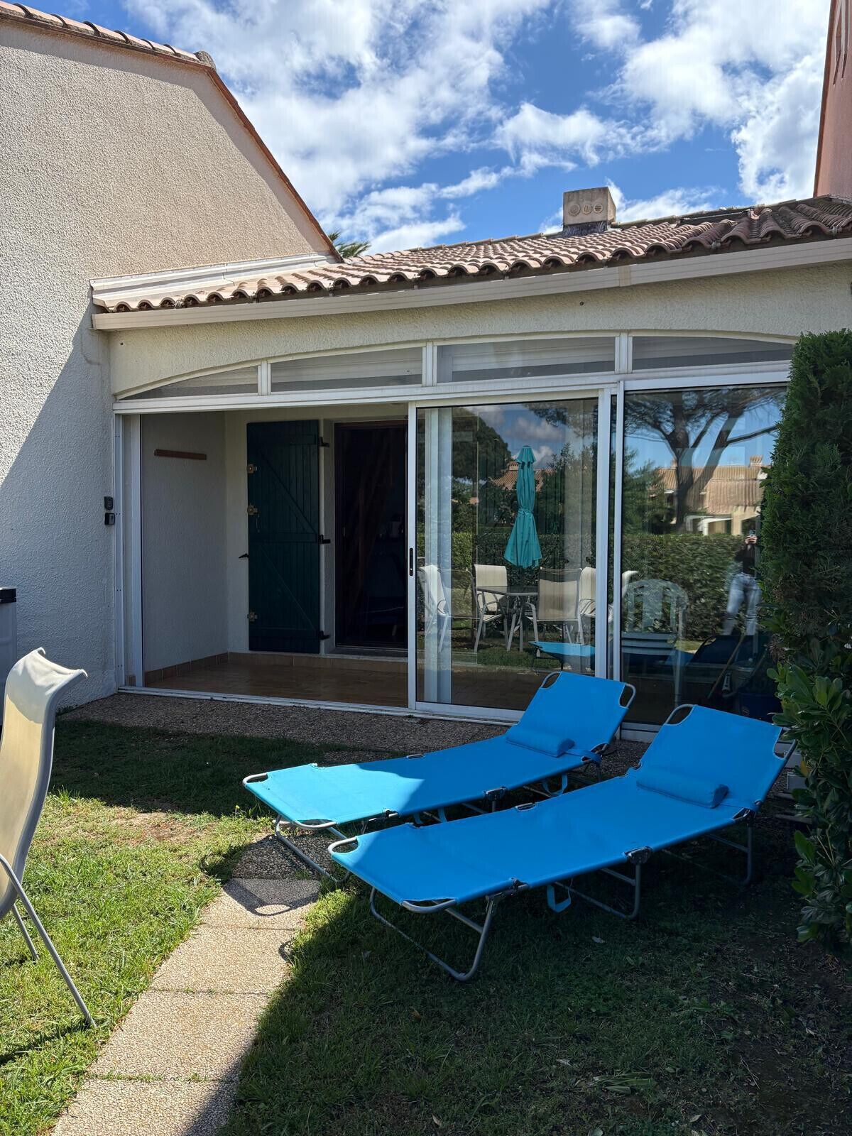Une maison dotée d’un patio comprenant deux fauteuils bleus et une porte vitrée donnant sur un espace extérieur aménagé avec une table et des chaises.