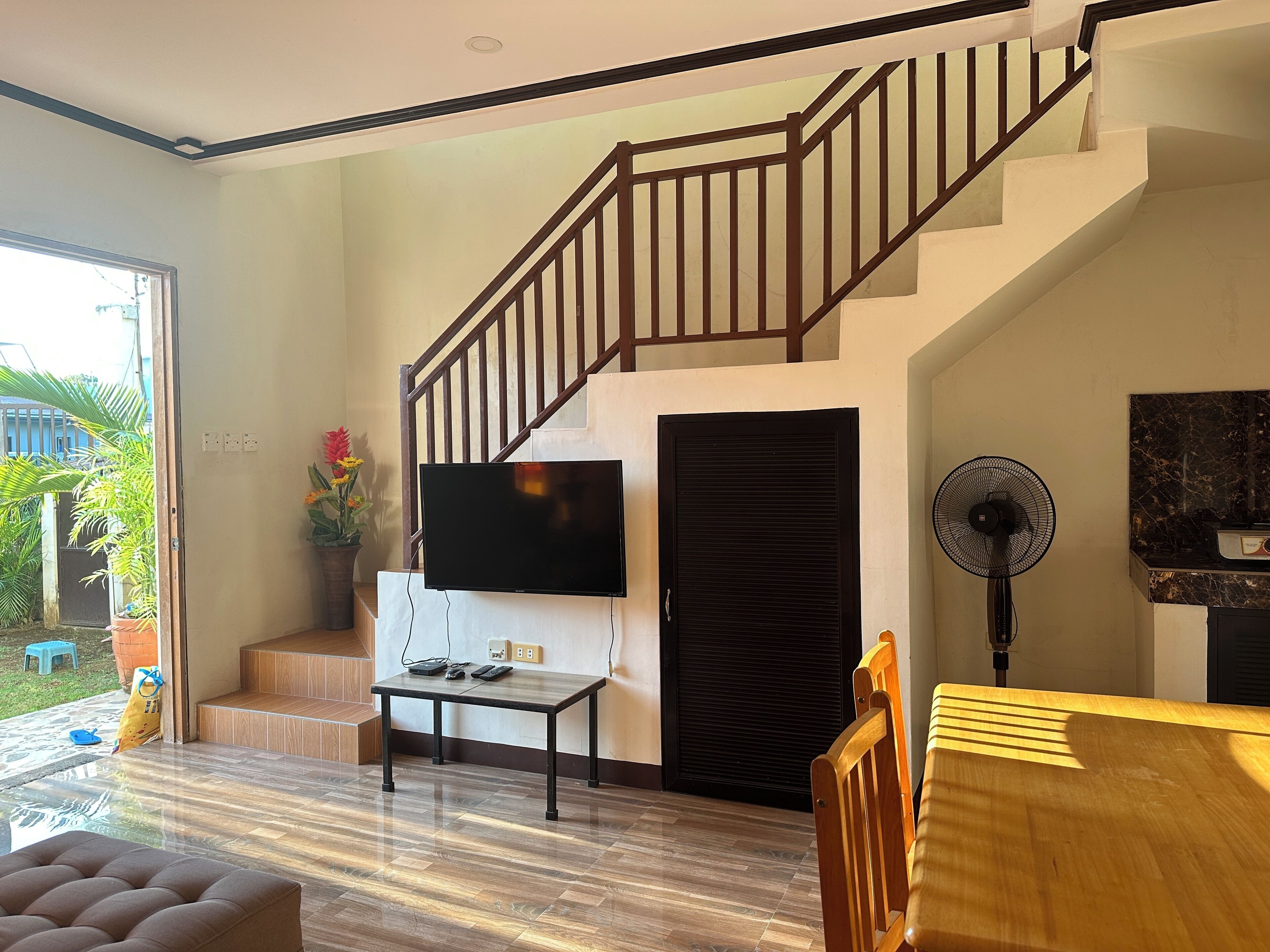 A modern living room with a staircase, a flat-screen TV, a fan, and a wooden coffee table.