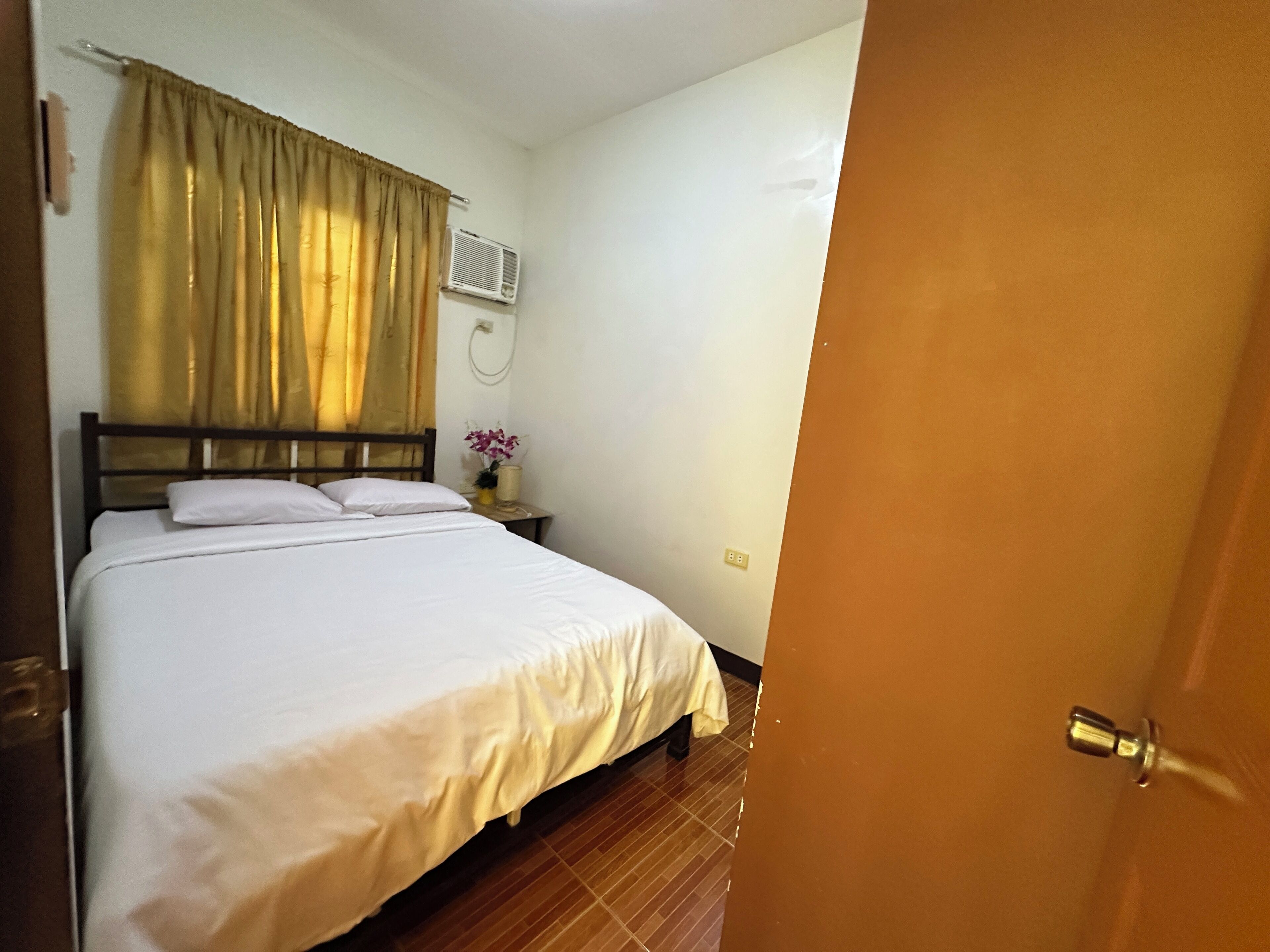 A hotel room with a bed, a nightstand, a wall-mounted air conditioner, and a door.