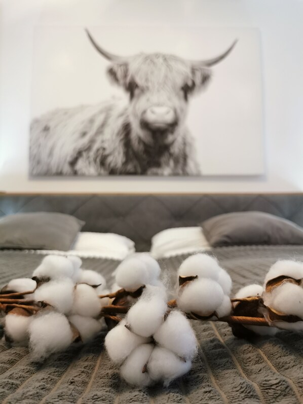 A bed with grey bedding, a framed black and white artwork of a bull, and a pile of cotton bolls in front of the bed.