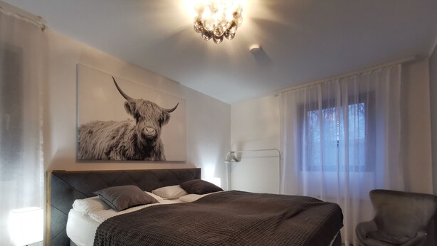 Une chambre à coucher moderne avec un grand lit, une œuvre d’art représentant un taureau accrochée au mur, une table de chevet avec une lampe et une chaise.