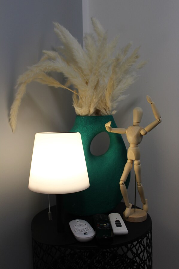 A lamp, a remote control, a phone, and a wooden mannequin on a black side table. - SmartApart - Designer Apartment - Prime Location - Fully Equipped - Public Transportation (Nürnberg)