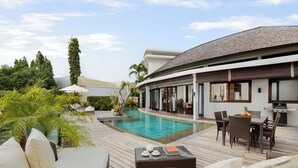A poolside area with a wooden deck, outdoor furniture, and a dining table.