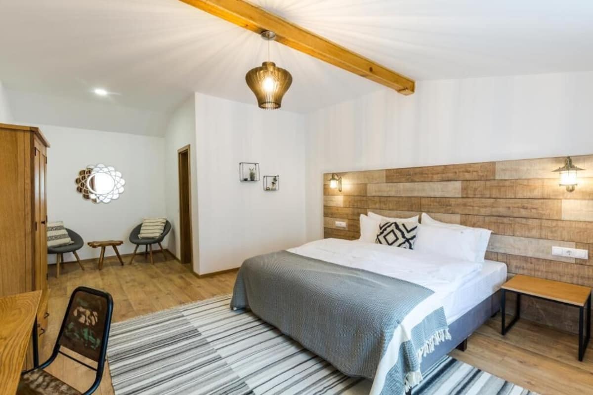 Ein Schlafzimmer mit hölzernem Kopfteil, einem Bett mit weißer Bettwäsche, einem Streifen Teppich, einer Holzbank und zwei Stühlen.