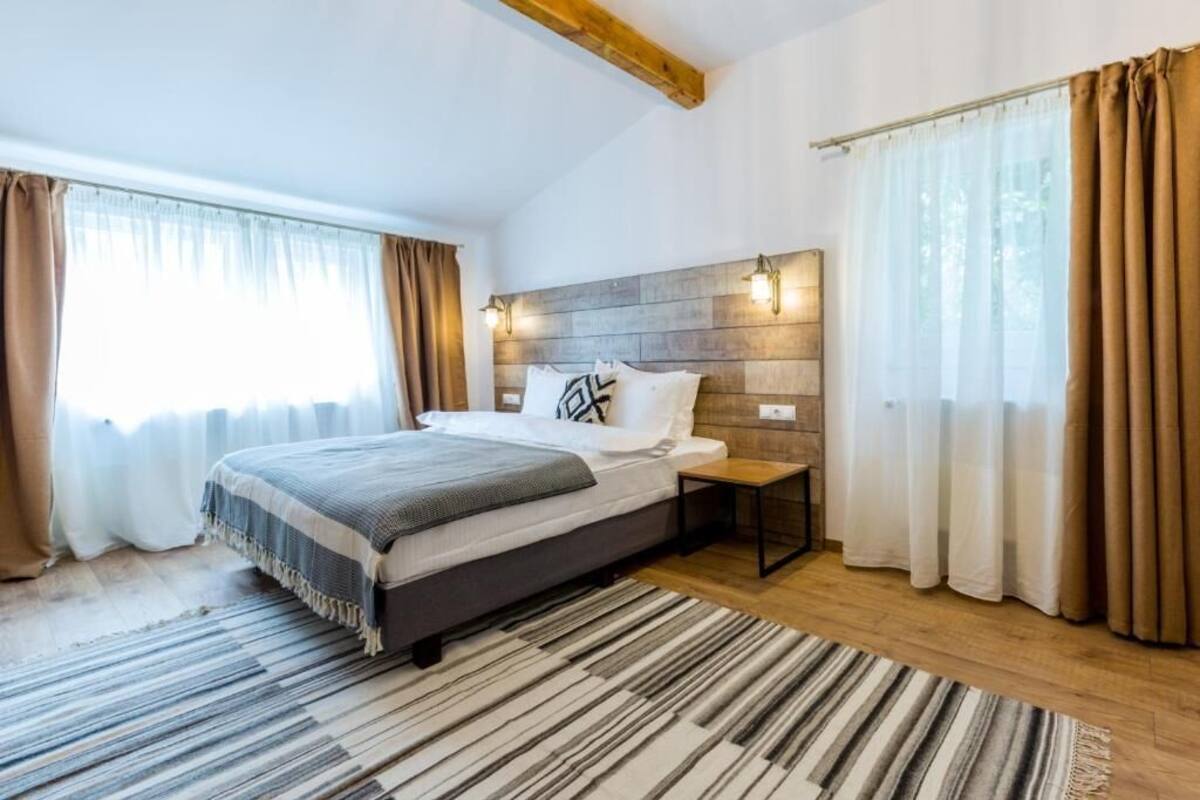 Ein Schlafzimmer mit einem Bett, einem Nachttisch, einem hölzernen Kopfstück und einem Fenster mit Vorhängen.