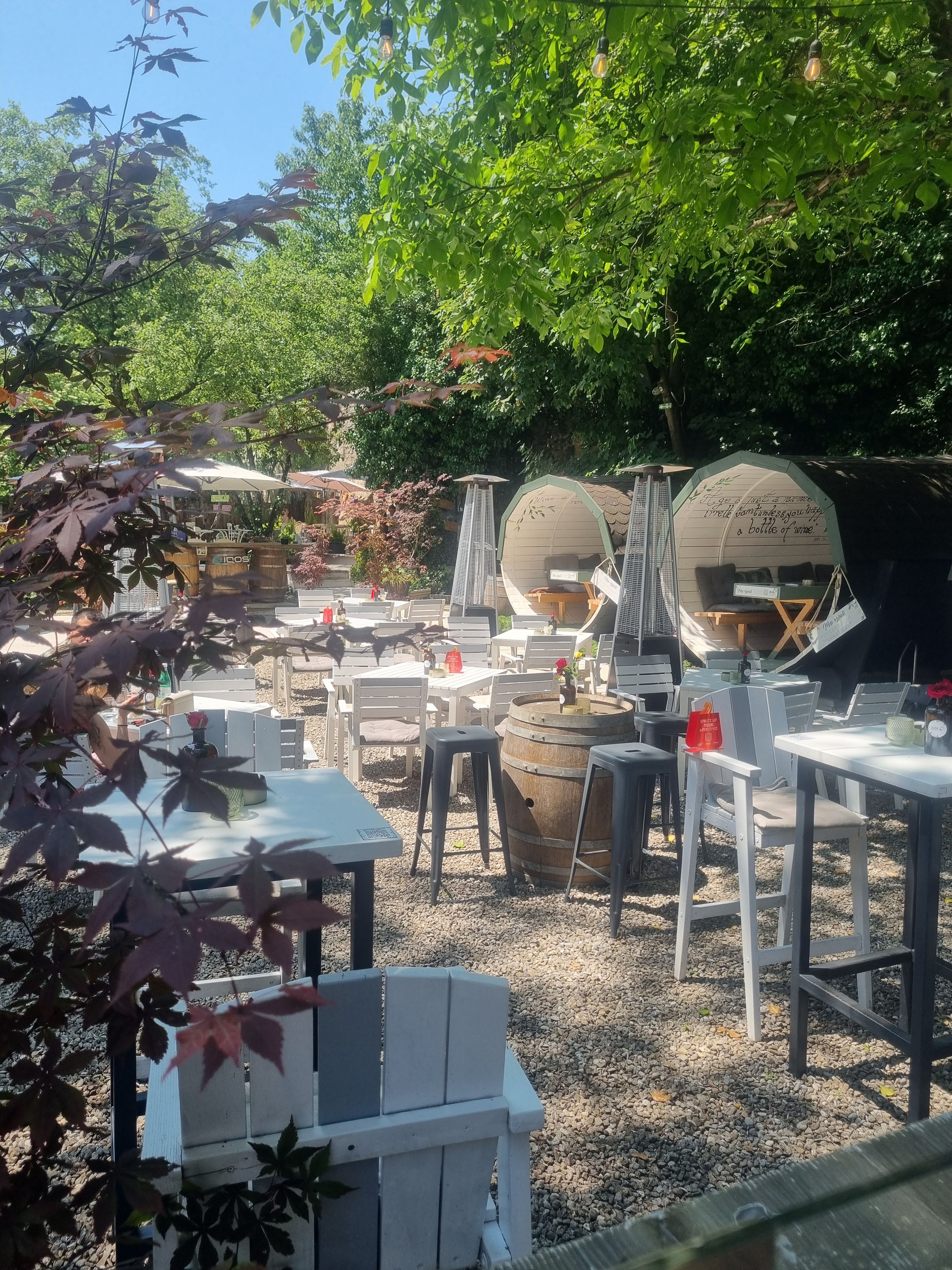 An outdoor seating area with tables and chairs, surrounded by greenery and trees.