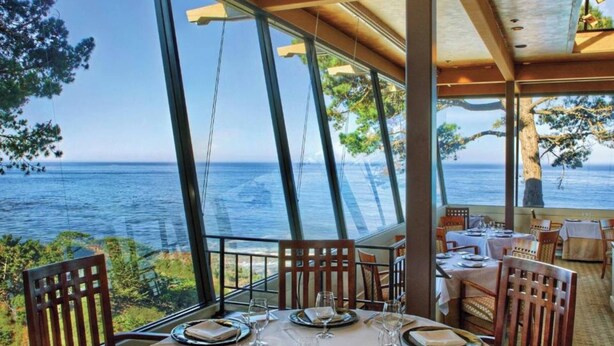 Un comedor con vista al mar, ventanas amplias y muebles de madera.