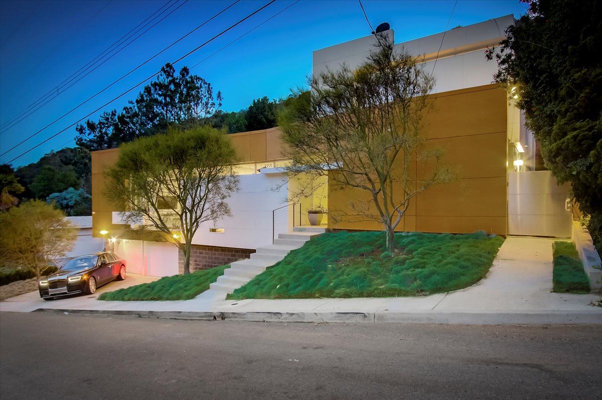 Una casa moderna con un coche estacionado en la entrada, un césped cuidado y un cielo despejado.
