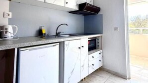 A compact kitchen with white marble cabinets, a built-in oven, and a small refrigerator. - Marina studios (Corfu)