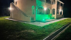A two-story building with a staircase on the left, a balcony on the upper floor, and a green-lit entrance. - Marina studios (Corfu)