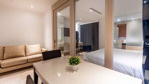 Una habitación de hotel moderna con sofá, una mesa de comedor con un florero, una cama y un espejo grande.