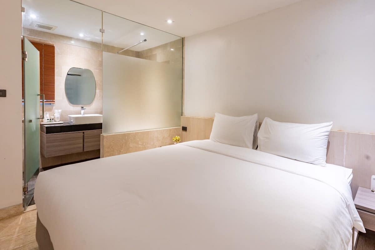 Une chambre d’hôtel moderne avec un grand lit, une salle de bain avec un miroir et une tête de lit en bois.