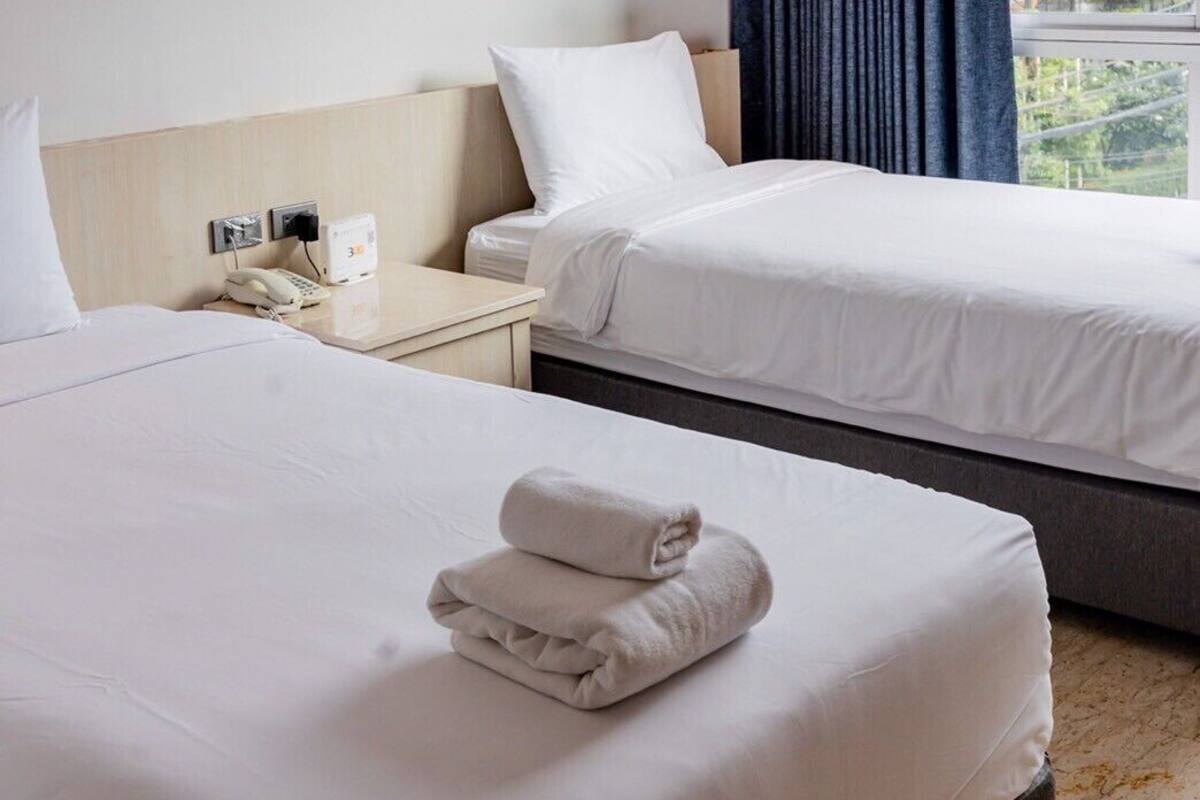 Une chambre d’hôtel avec deux lits, une table de chevet avec un téléphone et une fenêtre avec des rideaux.
