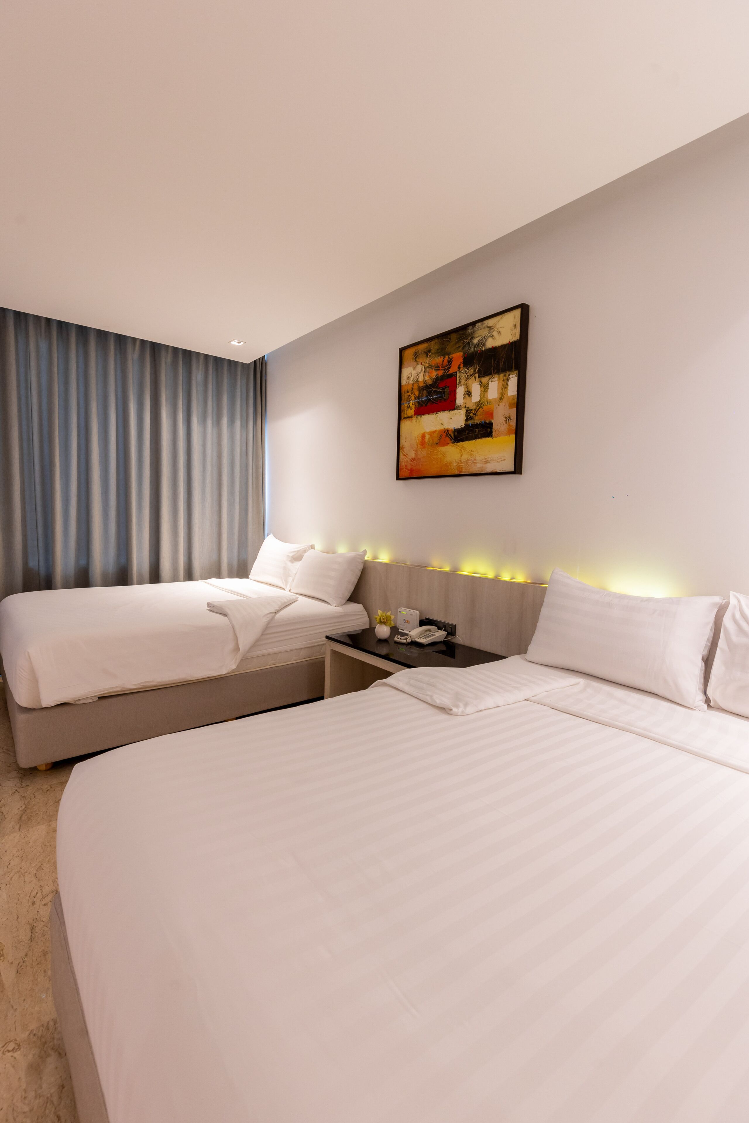 A hotel room with two beds, a bedside table with a phone, and a painting on the wall.