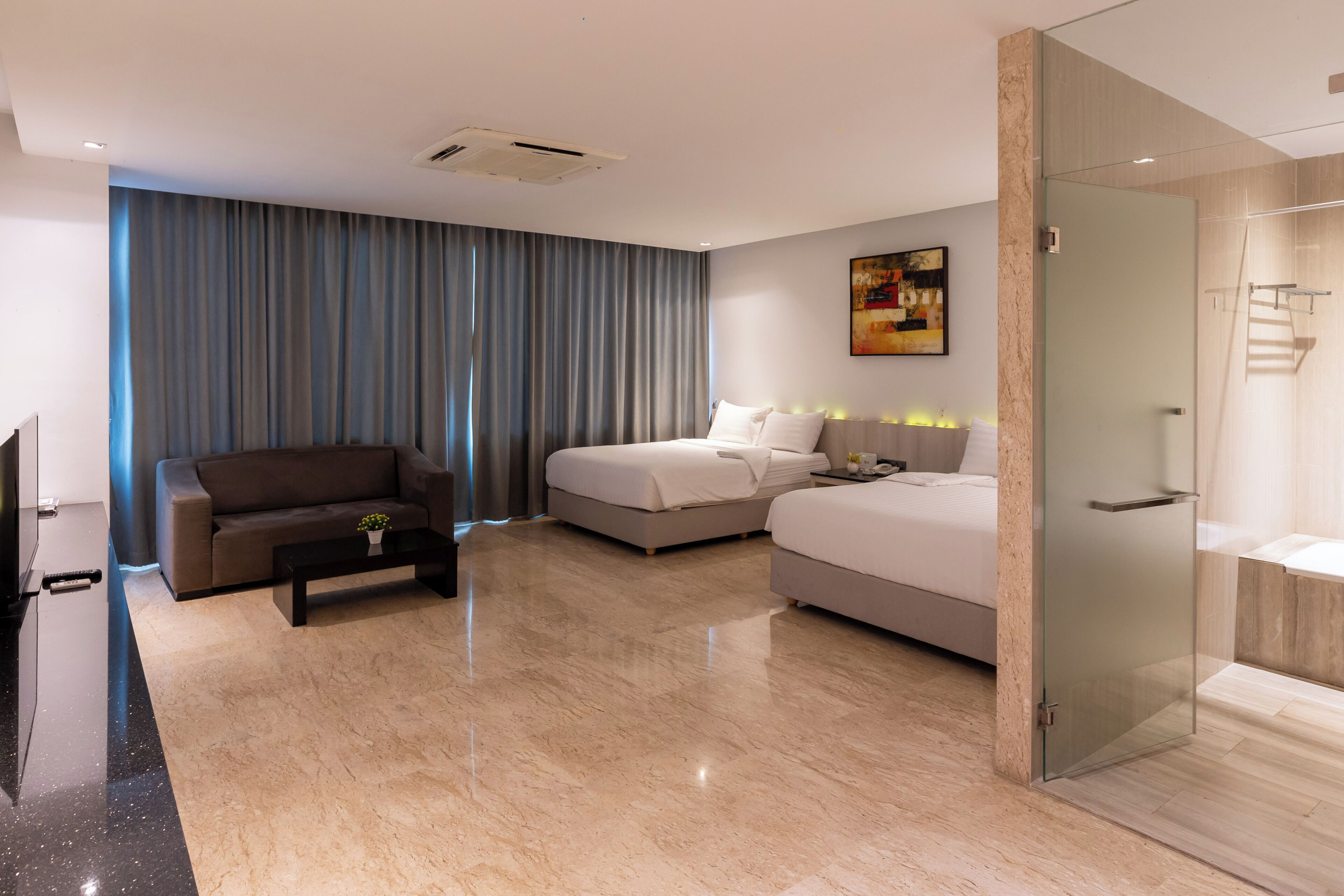 Una habitación de hotel moderna con sofá, cama, una mesita de centro y cabina de ducha de vidrio.