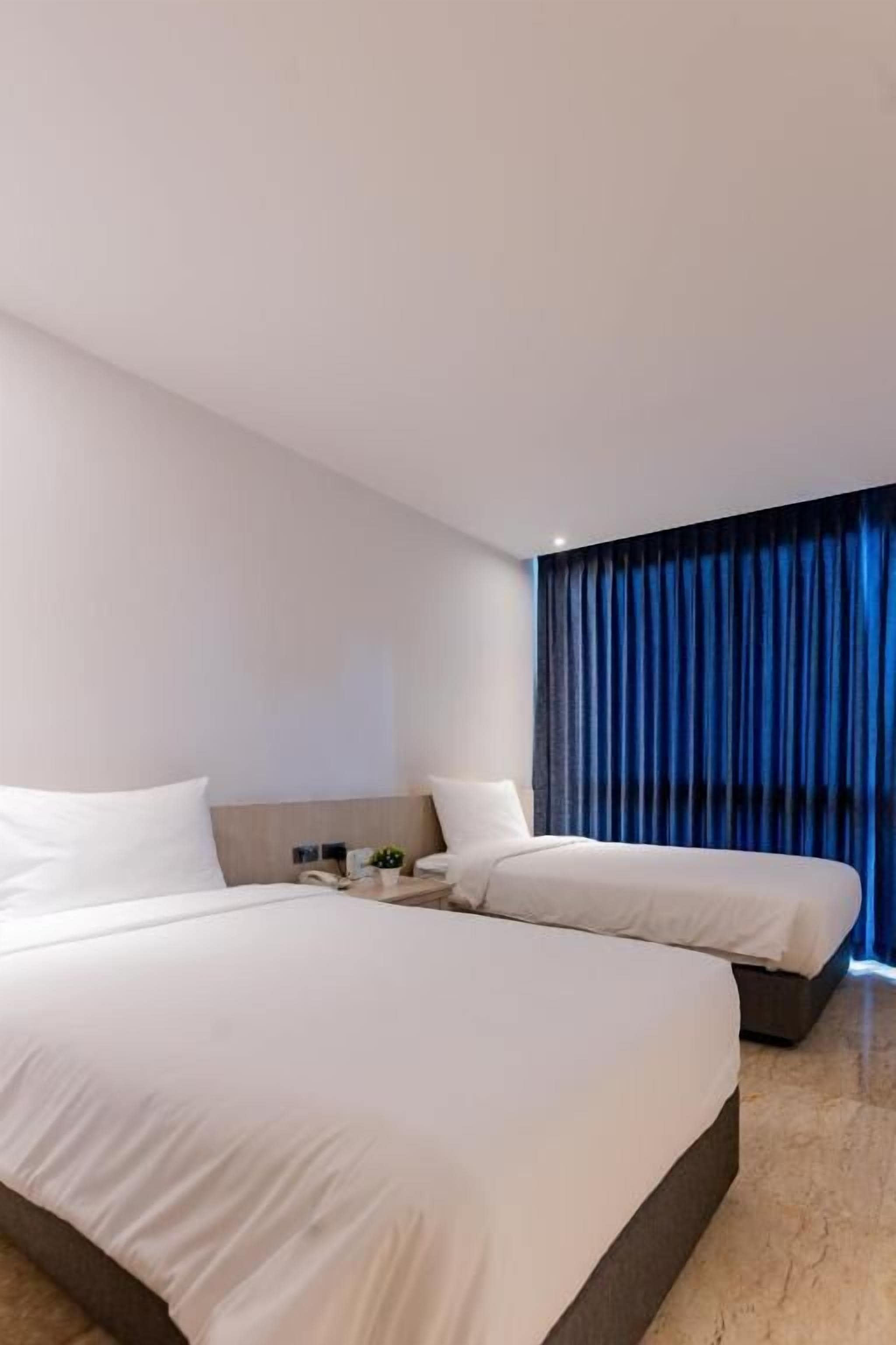 Una habitación de hotel moderna con dos camas, una mesita de noche y un ventanal con cortinas.