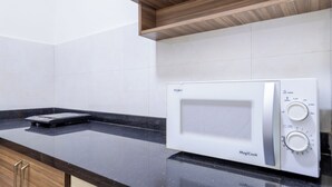 A kitchen with a microwave, a scale, and a wooden shelf above the counter.