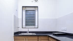A kitchen with a black countertop, wooden cabinets, a stainless steel sink, and a window with blinds.