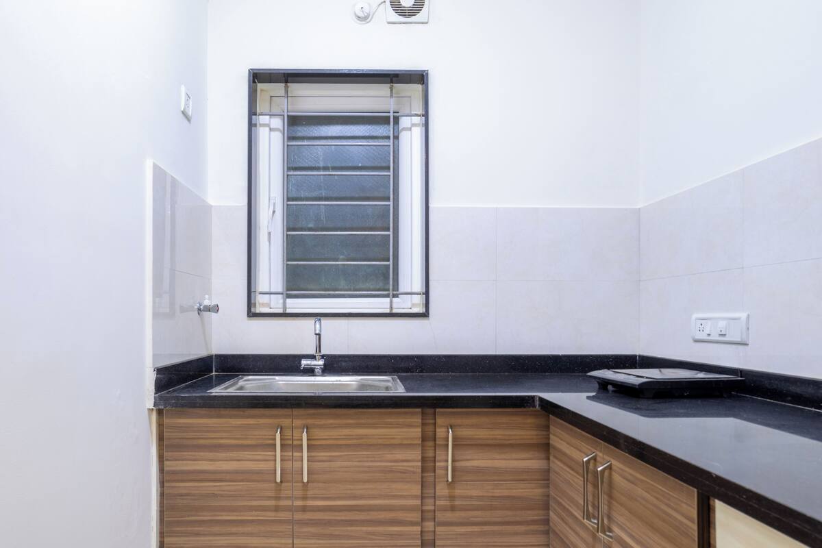 Eine Küche mit schwarzem Arbeitsplatz, Holzschränken, einer Spüle aus Edelstahl und einem Fenster mit Jalousien.